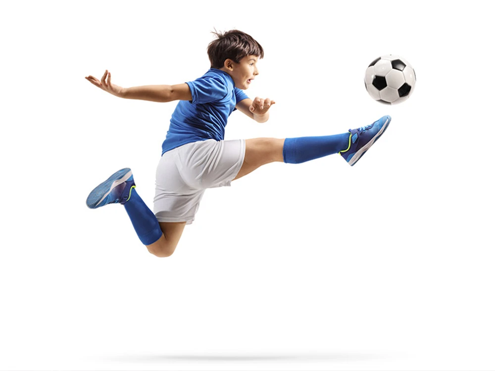 Young boy in soccer jersey jumping to kick soccer ball 