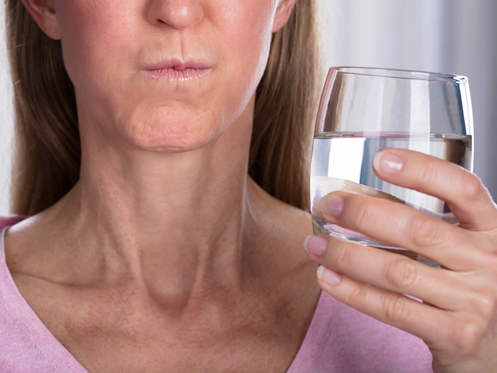 Woman holding glass of water while gargling 
