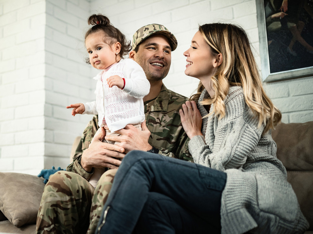 Man dressed in army uniform smiling with his wife and daughter