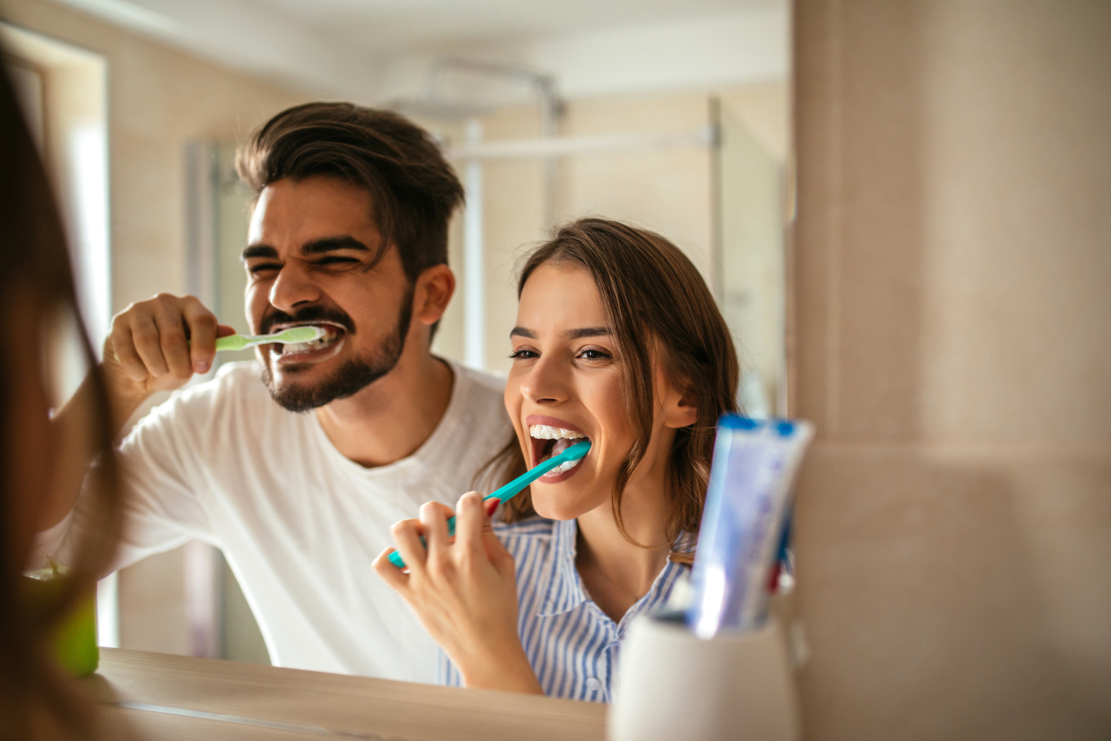 Couple Looking in bathroom mirror and brushing teeth