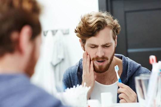 Man with beard holding toothbrush with sore tooth