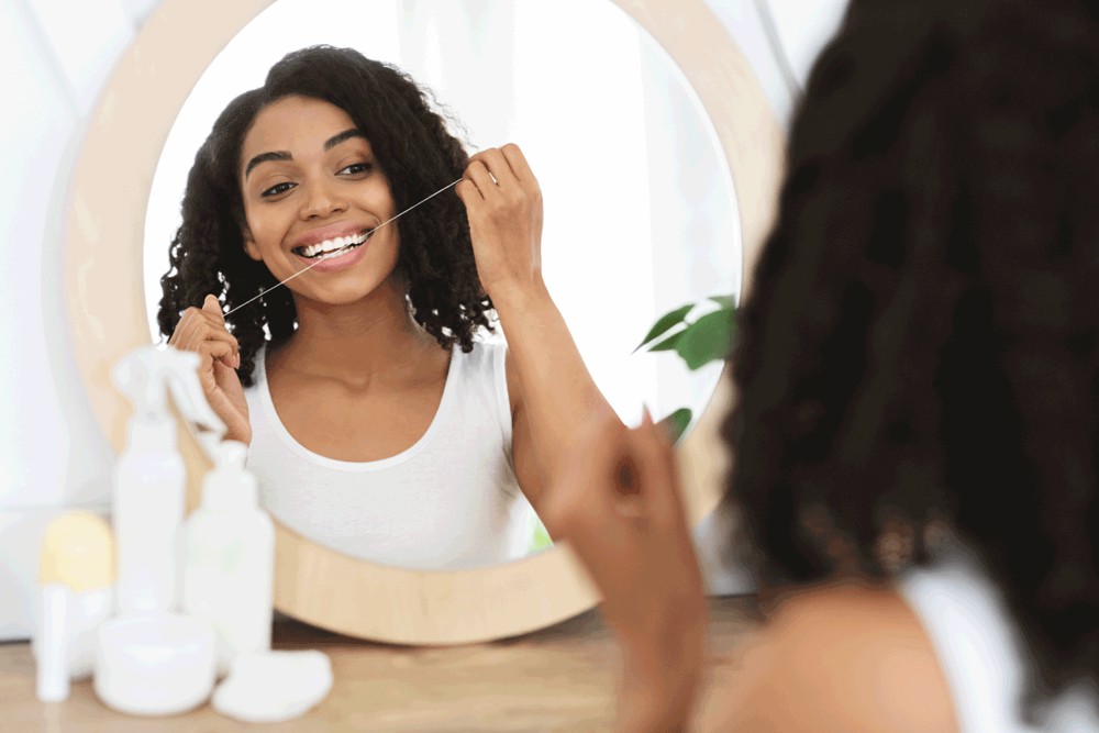 Woman looking in bathroom mirror flossing teeth 